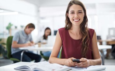 A female student sending a text on her cellphone while sitting with her textbooks